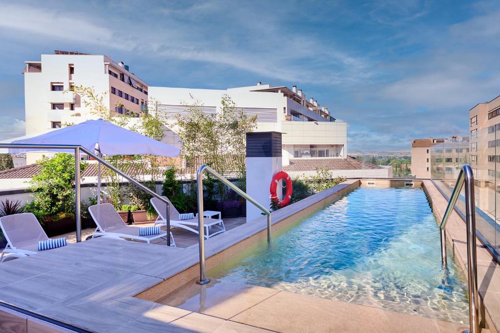 a swimming pool with two chairs and an umbrella at Apartamentos Luna Suites Granada in Granada