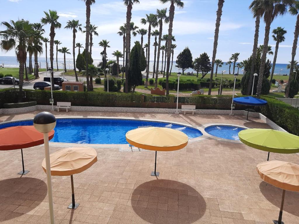 ein Pool mit Tischen und Stühlen und Palmen in der Unterkunft Apartamentos D&D VISTAMAR 1 línea in Castellón de la Plana