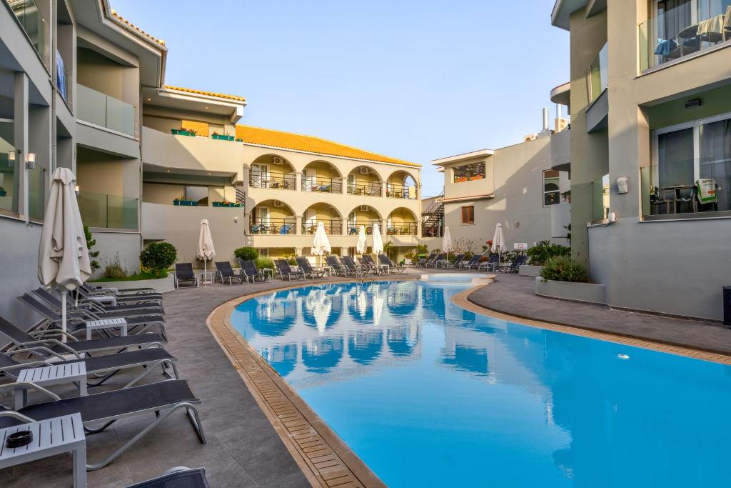 a hotel pool with chairs and umbrellas in a courtyard at White Olive Premium Laganas in Laganas