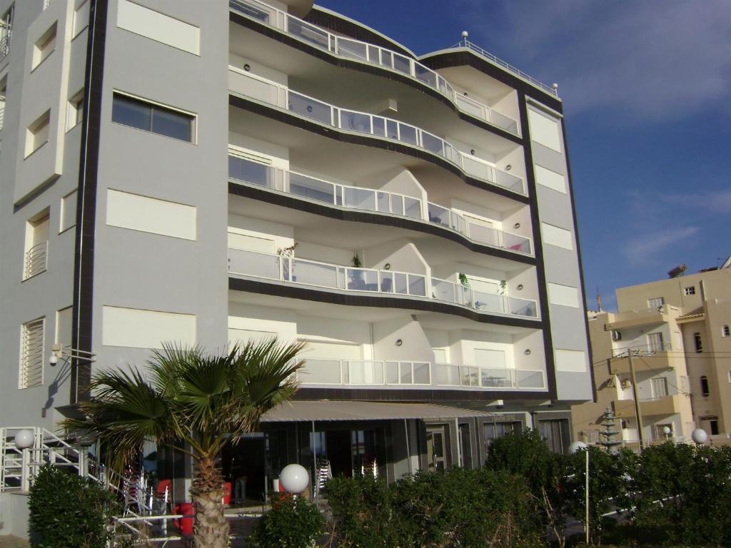 a tall white building with a palm tree in front of it at Studio Résidence Neptune Sousse Zone Kantaoui in Port El Kantaoui