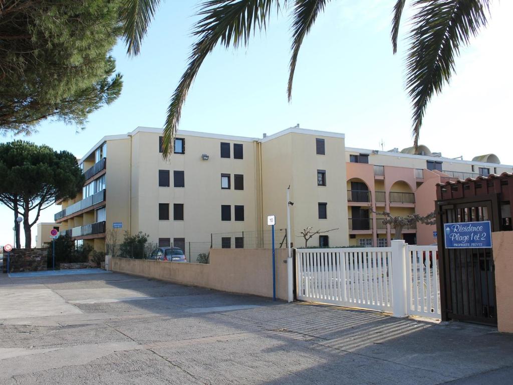 un bâtiment avec une clôture blanche et des palmiers dans l'établissement Appt cosy 4 pers, proche plage, parking - FR-1-229-769, à Gruissan