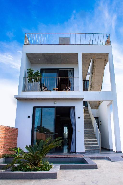 a white house with a balcony and stairs at CRIN HOUSE Đồng Châu in Lạc Thành