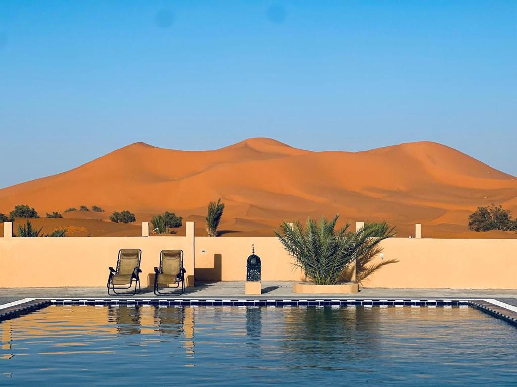 a swimming pool with two chairs and a desert at Hotel Camping Les Roses Des Dunes & Piscine in Merzouga