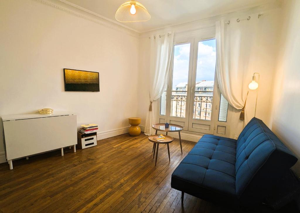 un salon avec un canapé bleu et une grande fenêtre dans l'établissement Appart coquet avec vue - Alesia, à Paris