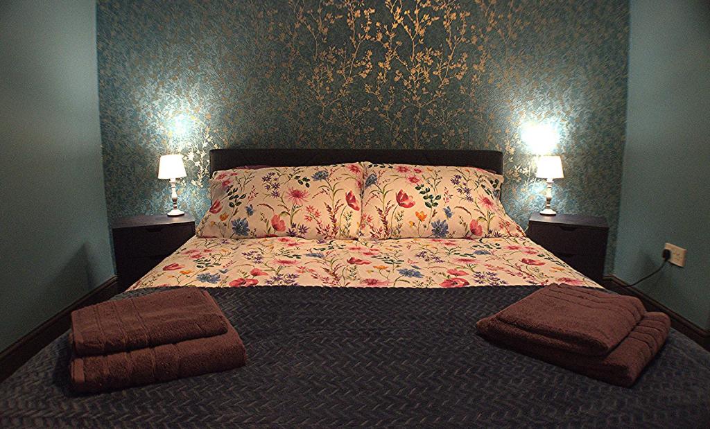 Hotel Dreamstay Apartments London Garden Central Tube Olympic, a bedroom with a bed with a floral bedspread and two lamps at Dreamstay Apartments London Garden Central Tube Olympic in London