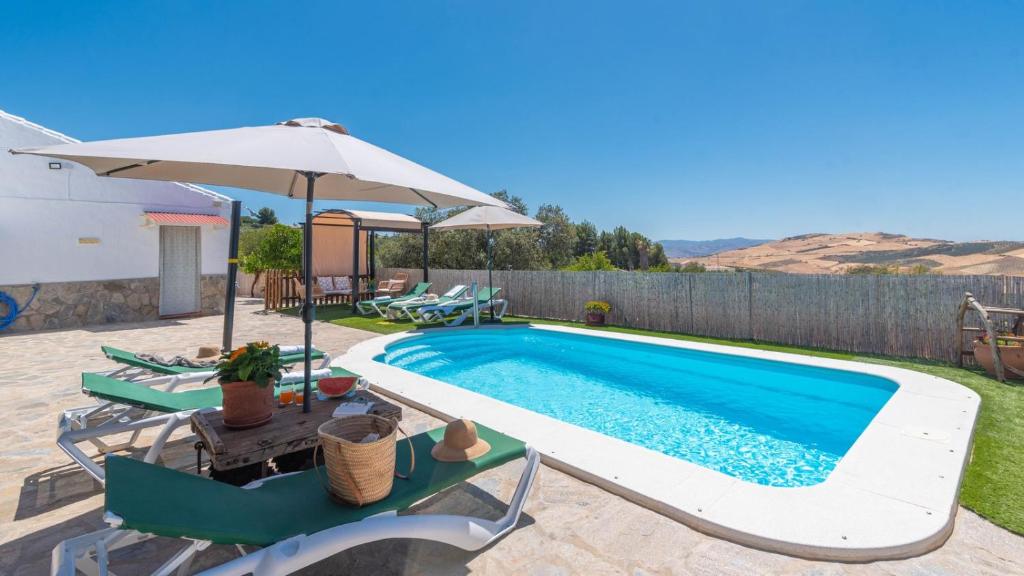 a swimming pool with chairs and an umbrella at Casa Pulirio Antequera - La Higuera by Ruralidays in Antequera