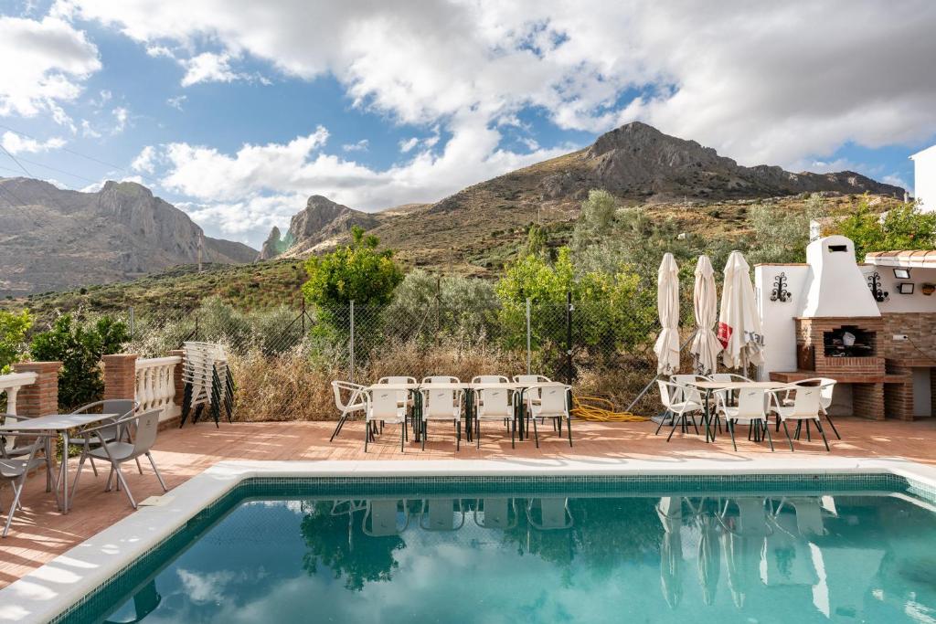 a pool with tables and chairs and mountains in the background at MalagaSuite Villa Rural Alcaucín in Alcaucín