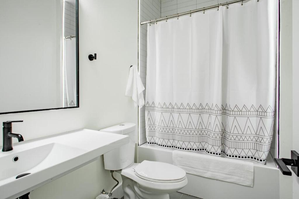 a white bathroom with a toilet and a shower curtain at Vibrant 2-BR Luxe Flat Adjacent Eastern Market Walk to METRO Barracks Row Capitol Hill in Washington, D.C.