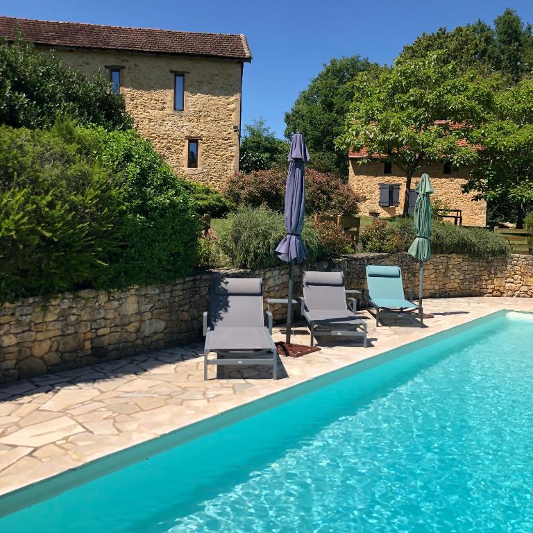 - une piscine avec des chaises et des parasols à côté d'un bâtiment dans l'établissement Les choses de la vie, à Saint-Alvère