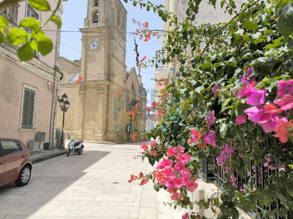 a building with a clock tower and pink flowers at Le Cementine Puglia On line in Morciano di Leuca