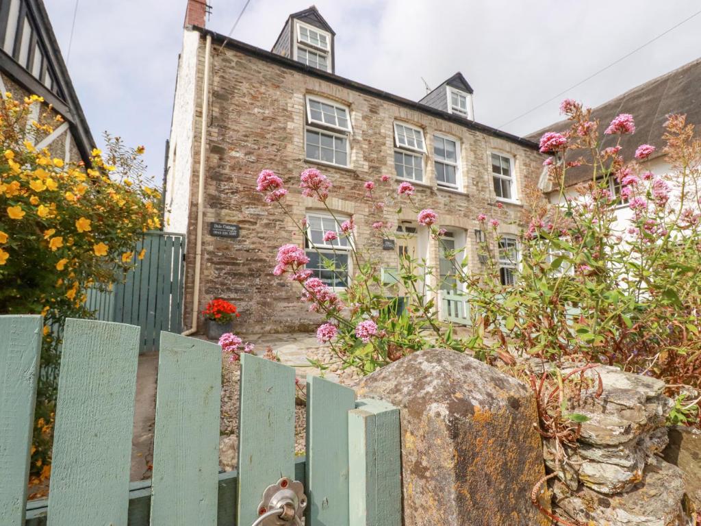 a brick building with pink flowers in front of a fence at Dale Cottage in Crantock