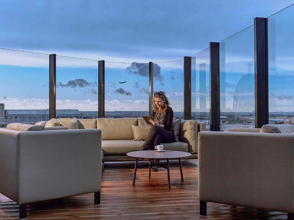 a woman sitting on a couch in a room with large windows at Pullman Paris Roissy Cdg Airport in Roissy-en-France