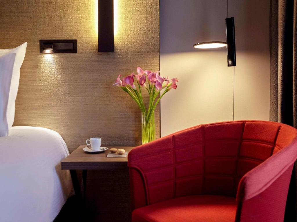 a room with a red chair and a vase of flowers at Pullman Paris Roissy Cdg Airport in Roissy-en-France