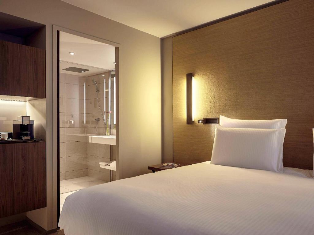 a bedroom with a large white bed and a bathroom at Pullman Paris Roissy Cdg Airport in Roissy-en-France