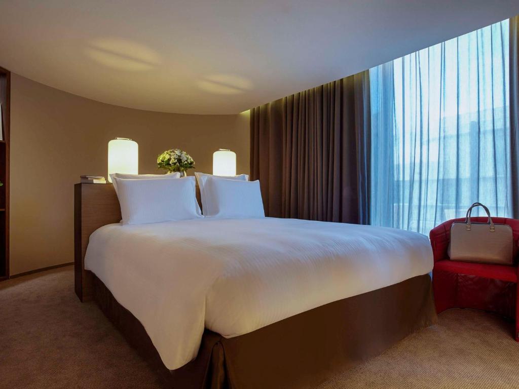 a hotel room with a large bed and a red chair at Pullman Paris Roissy Cdg Airport in Roissy-en-France