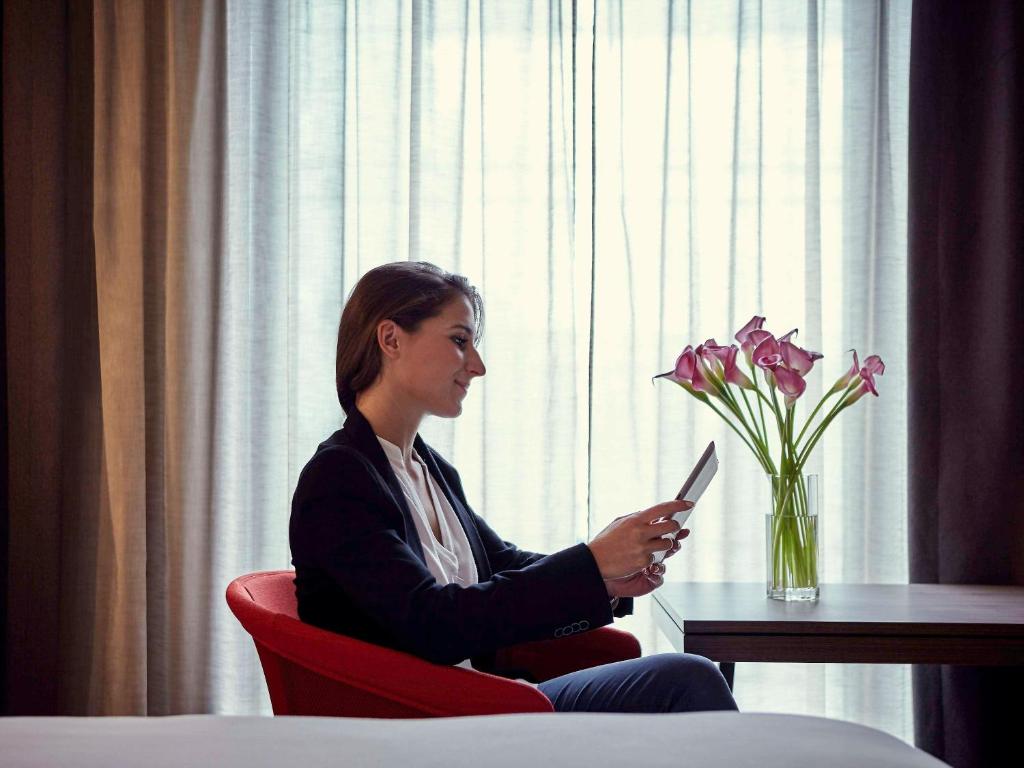a woman sitting in a red chair holding a cell phone at Pullman Paris Roissy Cdg Airport in Roissy-en-France