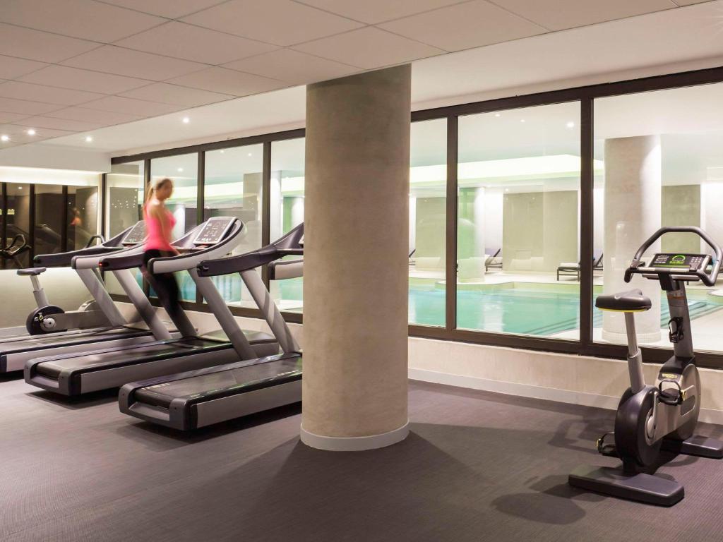 a woman running on treadmills in a gym with a swimming pool at Pullman Paris Roissy Cdg Airport in Roissy-en-France