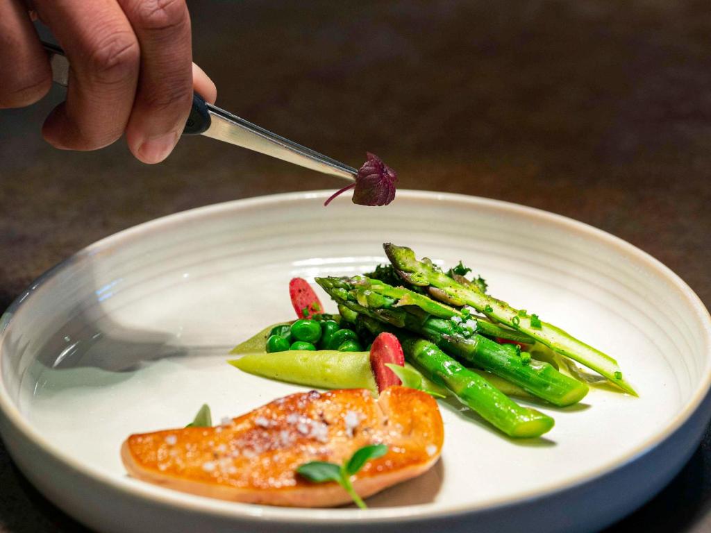 a person is eating food on a plate with vegetables at Pullman Paris Roissy Cdg Airport in Roissy-en-France