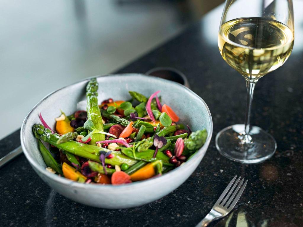a salad in a bowl next to a glass of wine at Pullman Paris Roissy Cdg Airport in Roissy-en-France