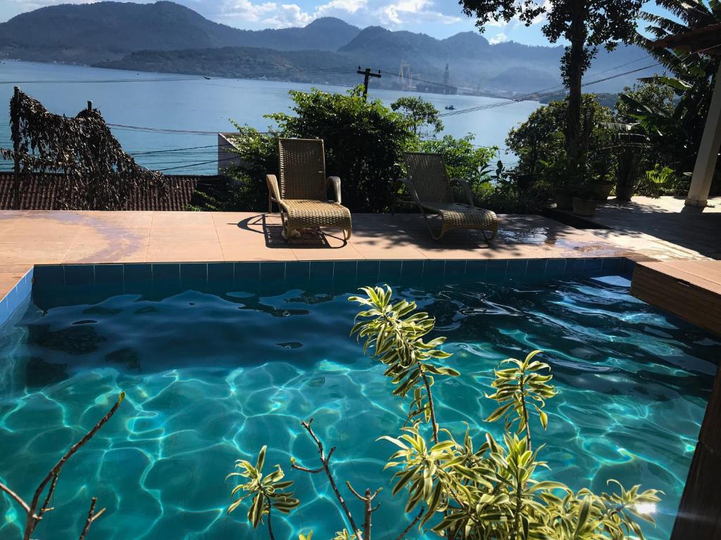 - une piscine avec 2 chaises et une vue sur l'eau dans l'établissement Casa com Piscina, Vista e Acesso ao Mar, à Angra dos Reis