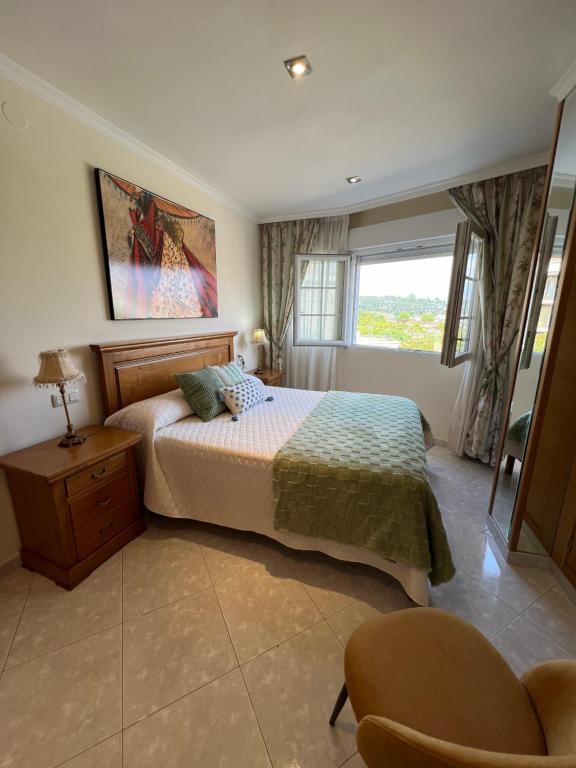 a bedroom with a bed and a chair and a window at Apartamento Arenal in Portonovo