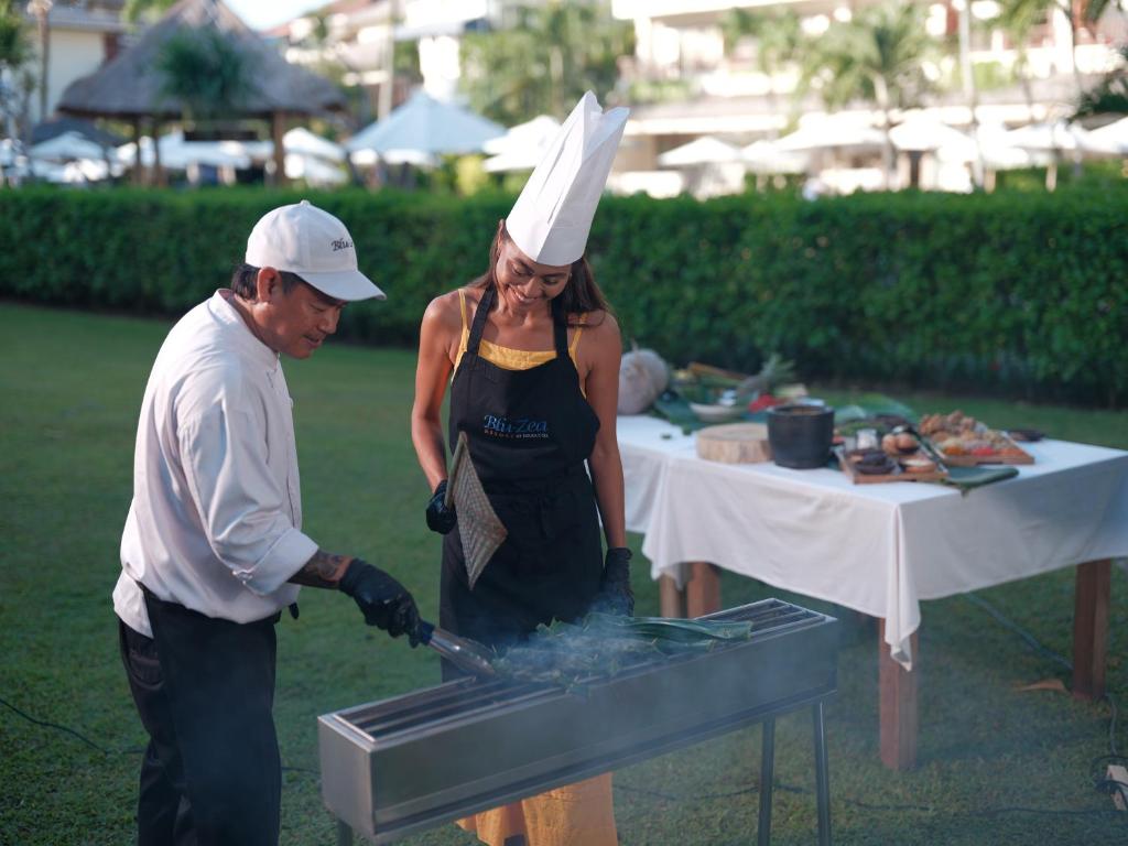 a man and a woman cooking food on a grill at Blu-Zea Resort by Double-Six in Seminyak
