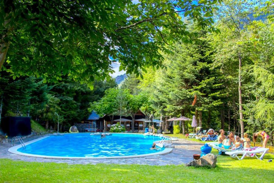 a swimming pool in a park with people sitting around it at Camping Bedura Park in Era Bordeta