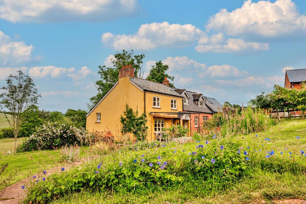 a yellow house in a field with purple flowers at Finest Retreats - Beili Glas Cottage in Penrhôs