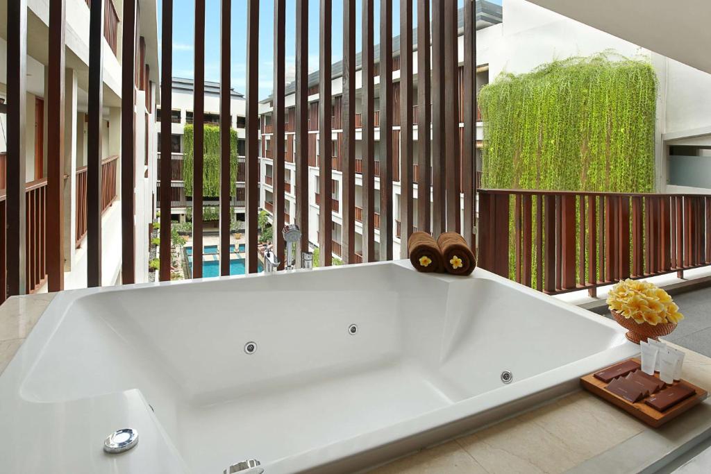 a large white bath tub in a room with a large window at The Magani Hotel and Spa in Legian