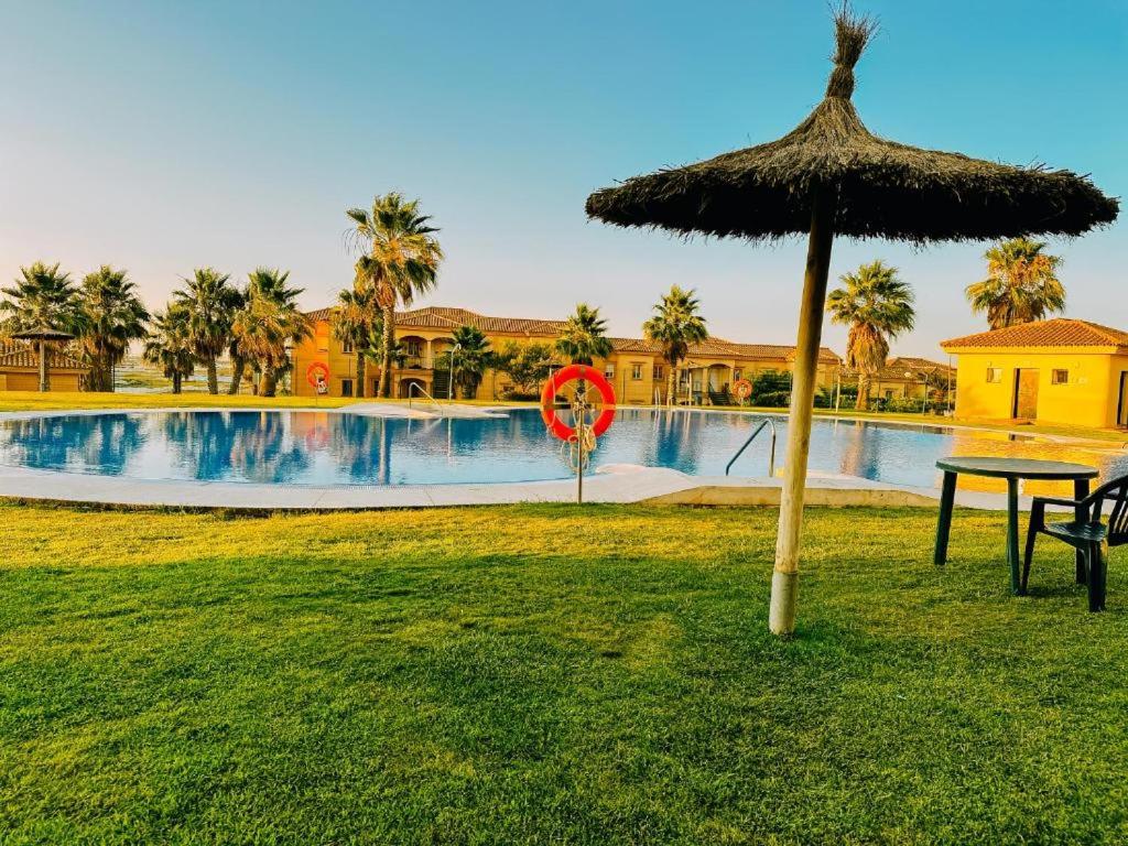 a table with a straw umbrella next to a swimming pool at Mika's House Valley in Sanlúcar de Barrameda