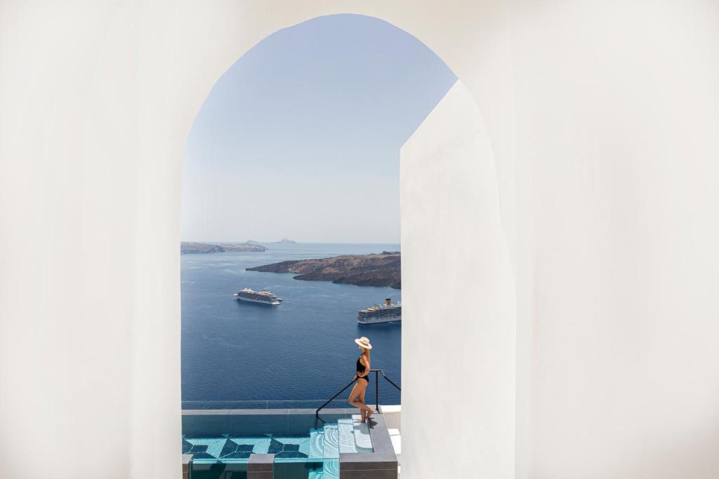 una donna che cammina sul bordo di un edificio con vista sull'oceano di CASASUNSHA Hybrid Retreat Santorini a Firà