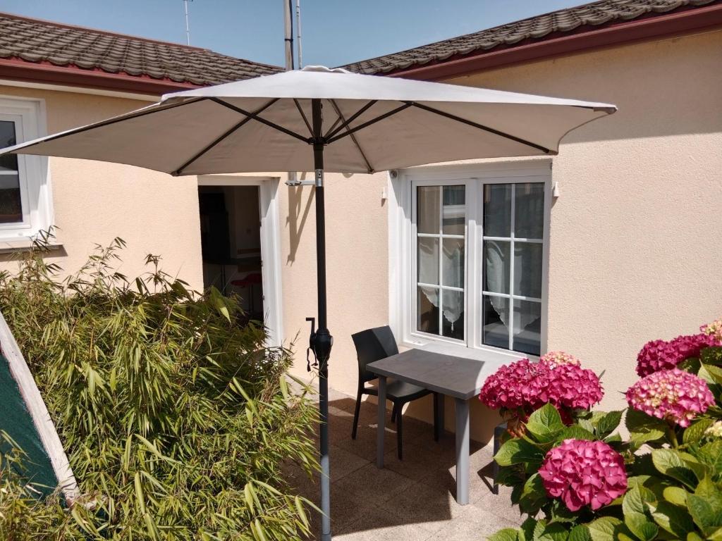 un parasol blanc sur une terrasse avec des fleurs roses dans l'établissement Les Hortensias, à Challans