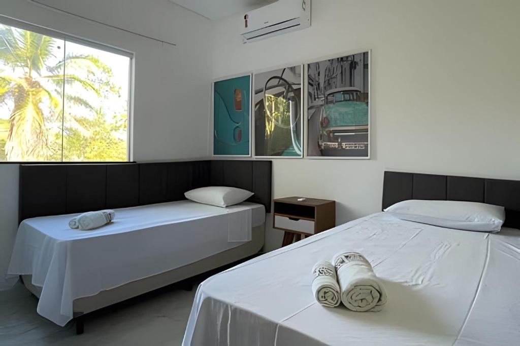 two beds in a room with white sheets and a window at AP 15 - 500m da BEIRA MAR de Taperapuan, 2 quartos in Porto Seguro
