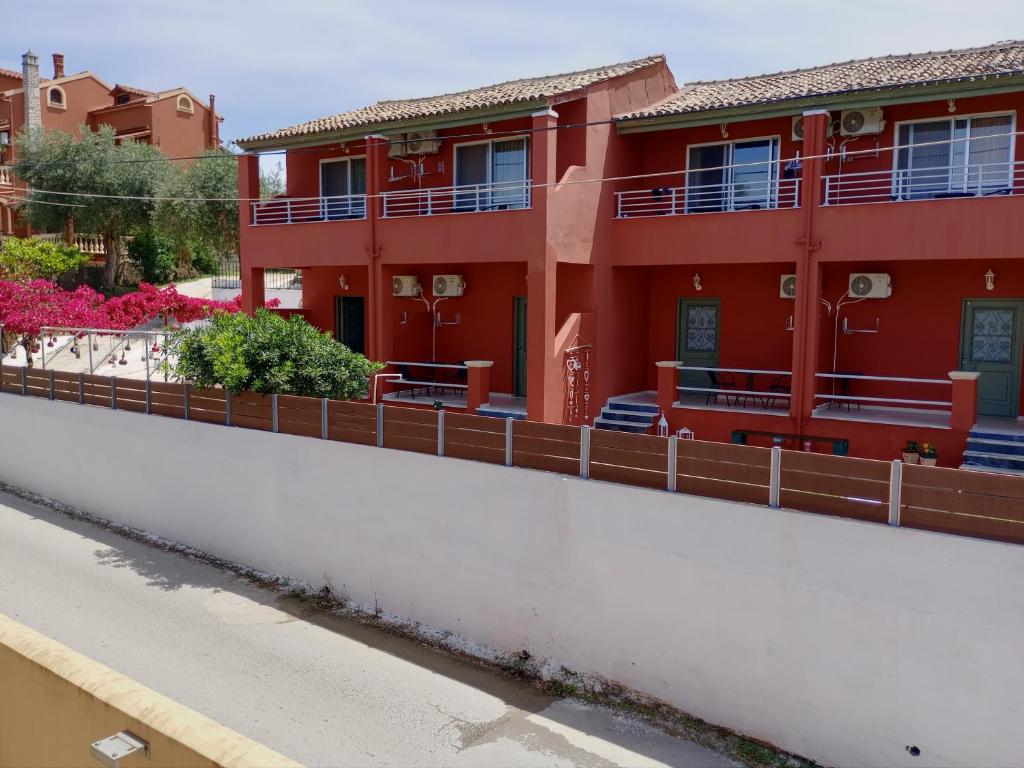 czerwony budynek z płotem obok ulicy w obiekcie maria corfu apartments w mieście Mesongi