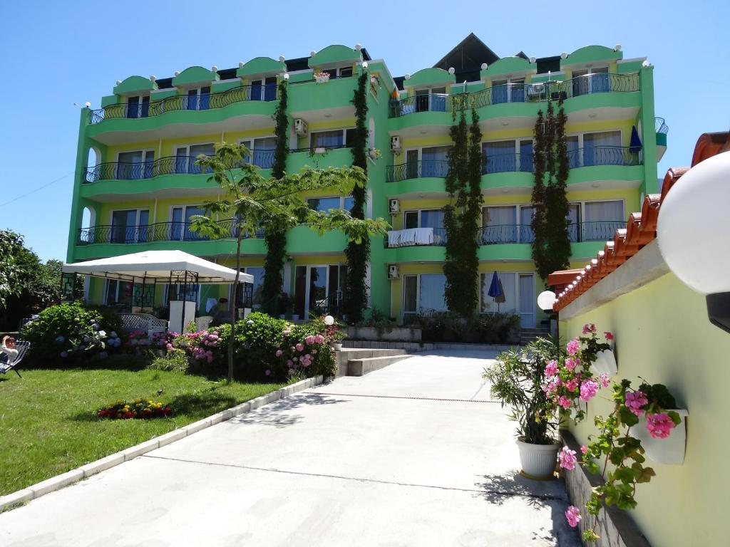 a large yellow building with trees and flowers at Guesthouse Kamelia in Ahtopol