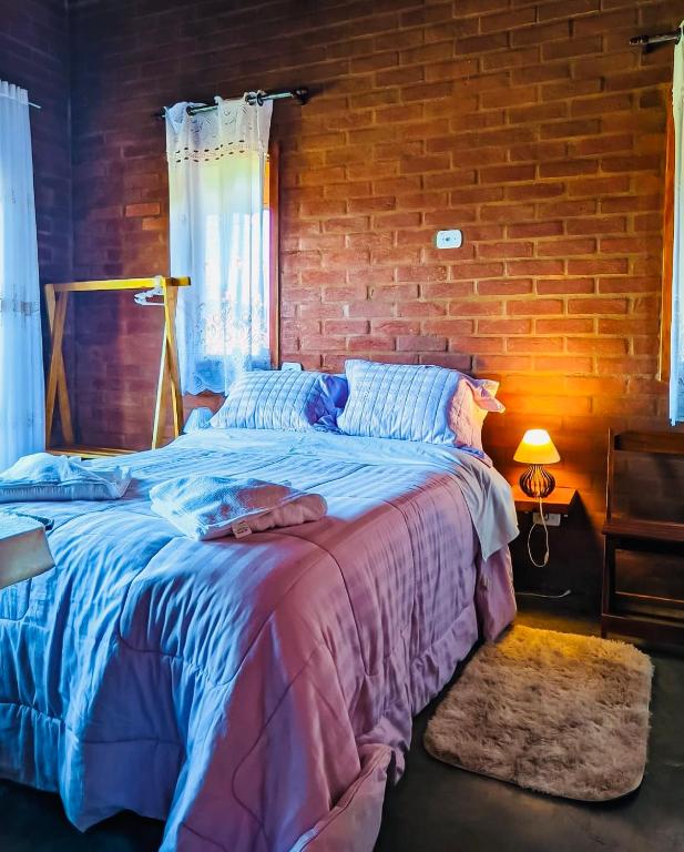 a bedroom with a large bed with a brick wall at Chalé Caminho das Flores in Santo Antônio do Pinhal