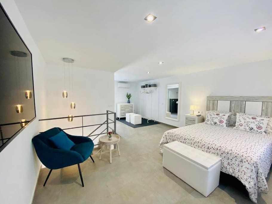 a white bedroom with a bed and a blue chair at IV Apartamentos Morales & Arnal in Ronda