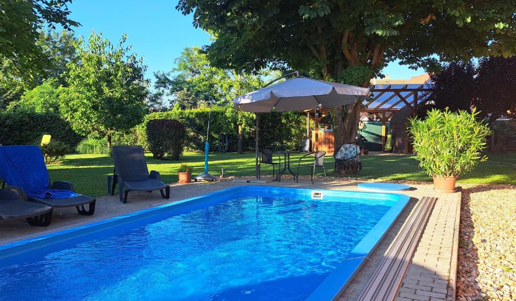 a blue swimming pool with chairs and an umbrella at Diófa Vendégházak in Tiszafüred