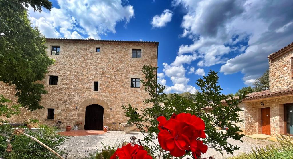 a brick building with red flowers in front of it at Hotel Mas Pelegri in Serinyà