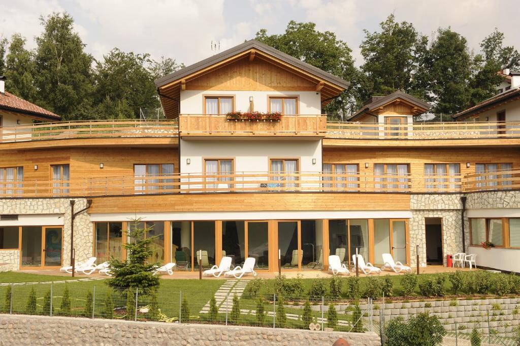 a large wooden house with a deck and chairs at Hotel Belvedere Wellness & Family in Baselga di Pinè
