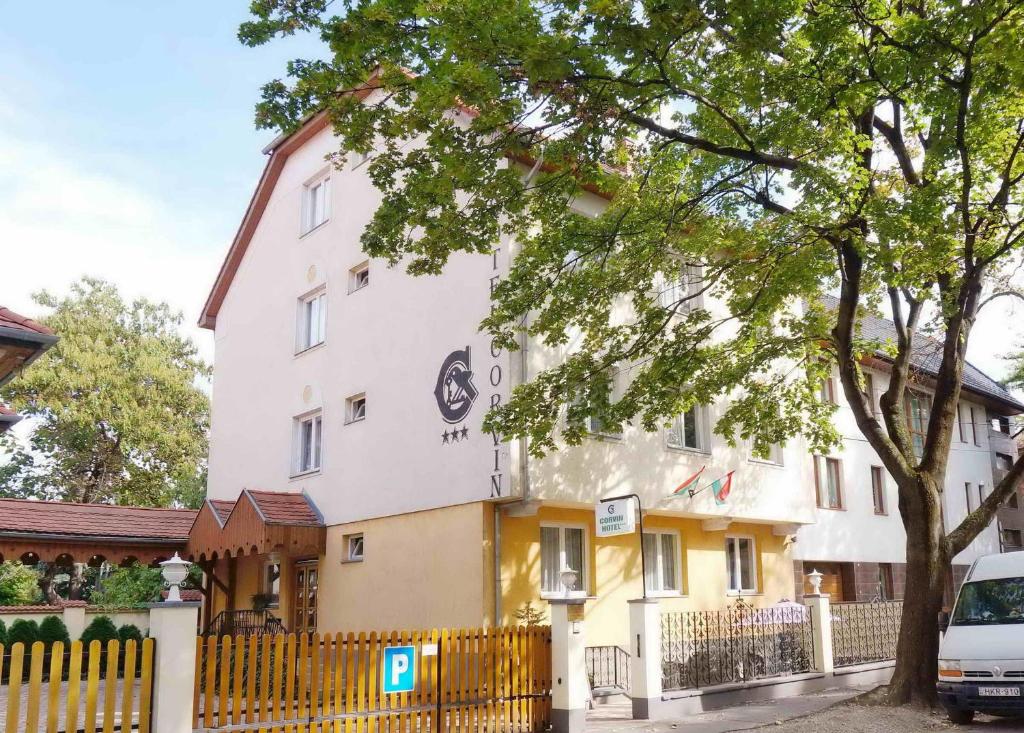 Ein weißes Gebäude mit einem Zaun davor. in der Unterkunft Corvin Hotel in Győr