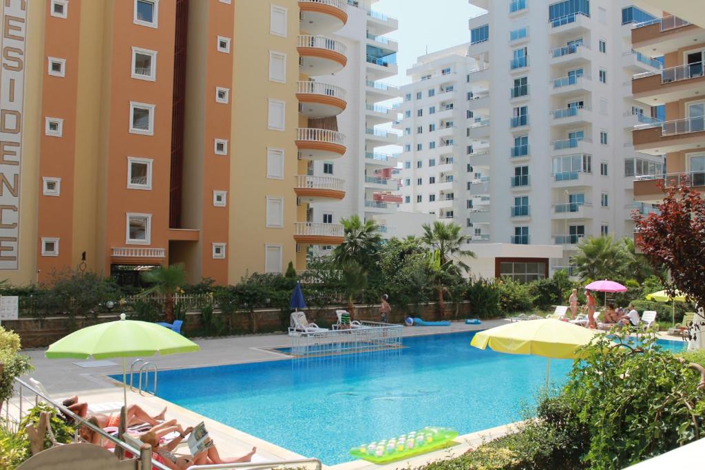a swimming pool with chairs and umbrellas next to tall buildings at Apartment Toros Cekic in Mahmutlar