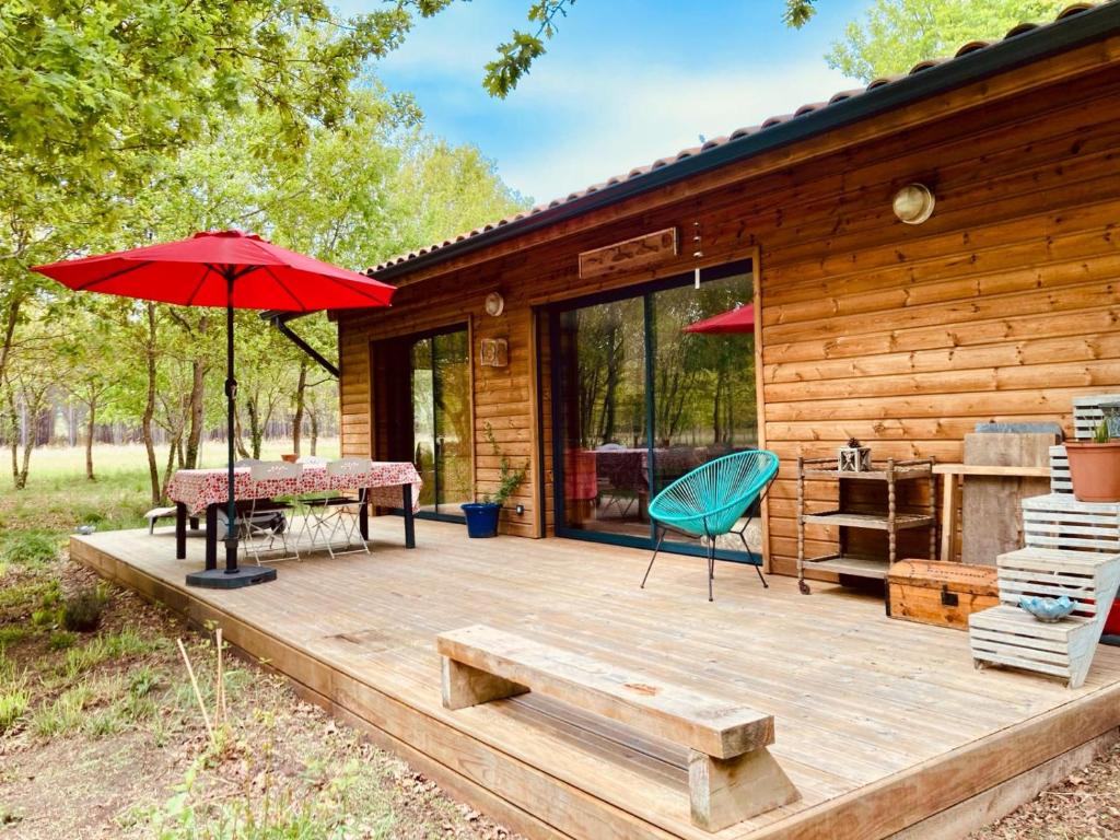une terrasse en bois avec une table et un parasol rouge dans l'établissement Eco-Friendly Boho Loft Chalet, à Saint-Julien-en-Born