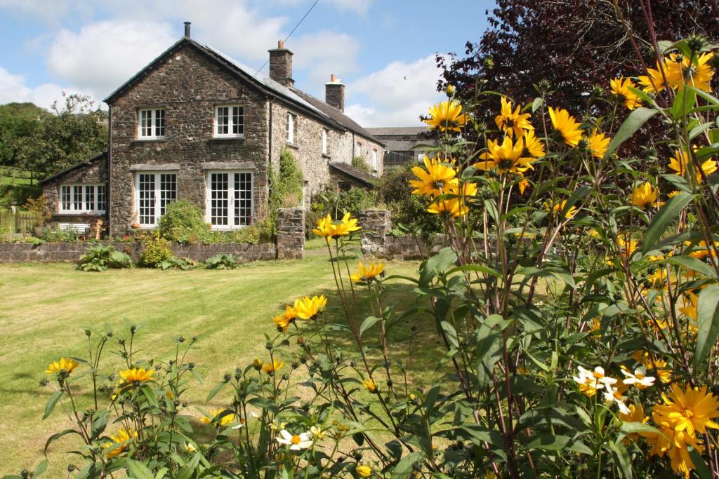 una vieja casa de piedra con flores amarillas delante de ella en Holdstrong Farmhouse, en Lydford