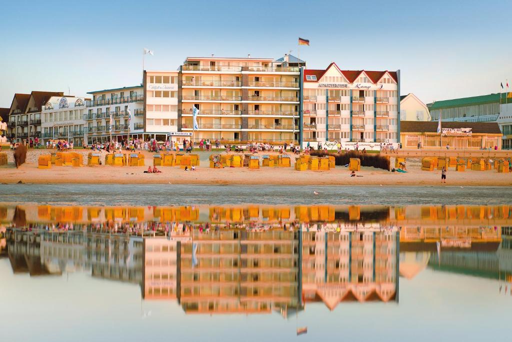a group of buildings on a beach with a reflection in the water at Strandhotel Duhnen in Cuxhaven