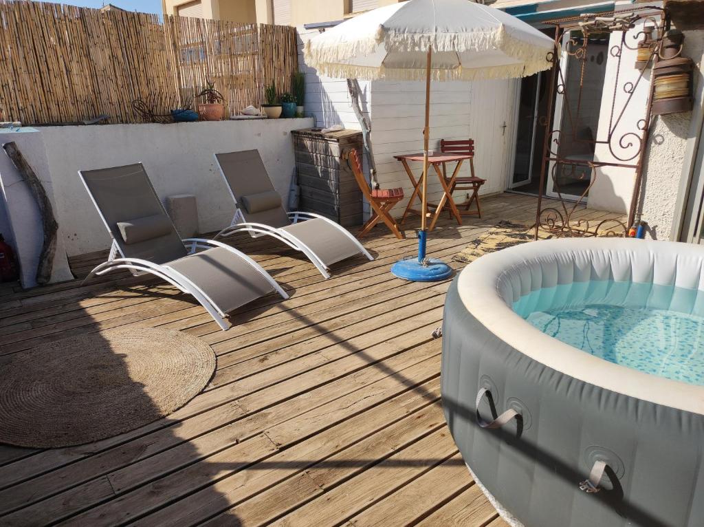 une terrasse avec un bain à remous, des chaises et un parasol dans l'établissement Chambre cabane de charme, terrasse et spa privé, à Valras-Plage