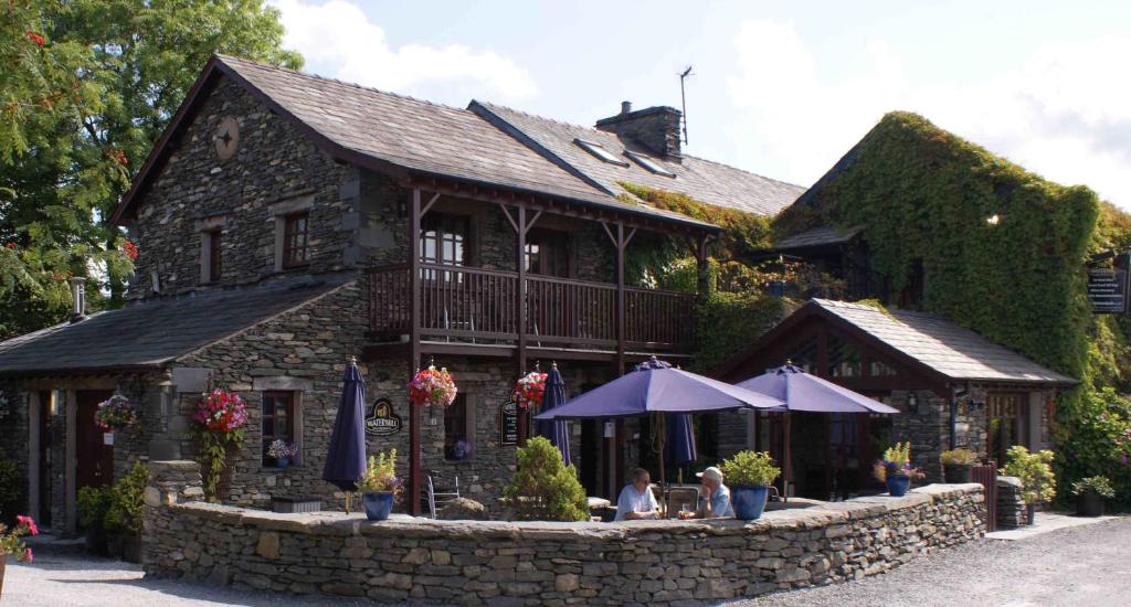 un edificio con dos personas sentadas bajo sombrillas frente a él en The Watermill Inn & Brewery en Windermere