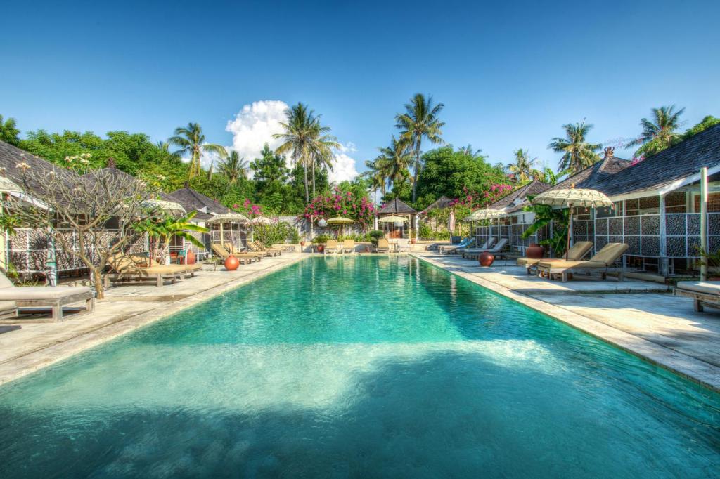 a swimming pool at a resort with palm trees at Les Villas Ottalia Yoga & Diving, Gili Meno in Gili Meno
