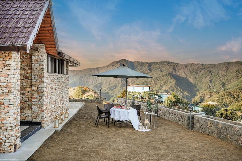 a table with an umbrella on a balcony with mountains at SaffronStays Ridgeview Manor, Mukteshwar - 3BHK Villa with Himalayan Views & Verandahs in Mukteshwar