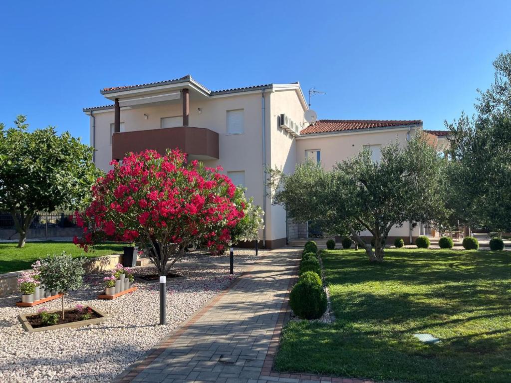 ein Haus mit einem Garten mit rosa Blumen und Bäumen in der Unterkunft Apartments Maric in Vodice